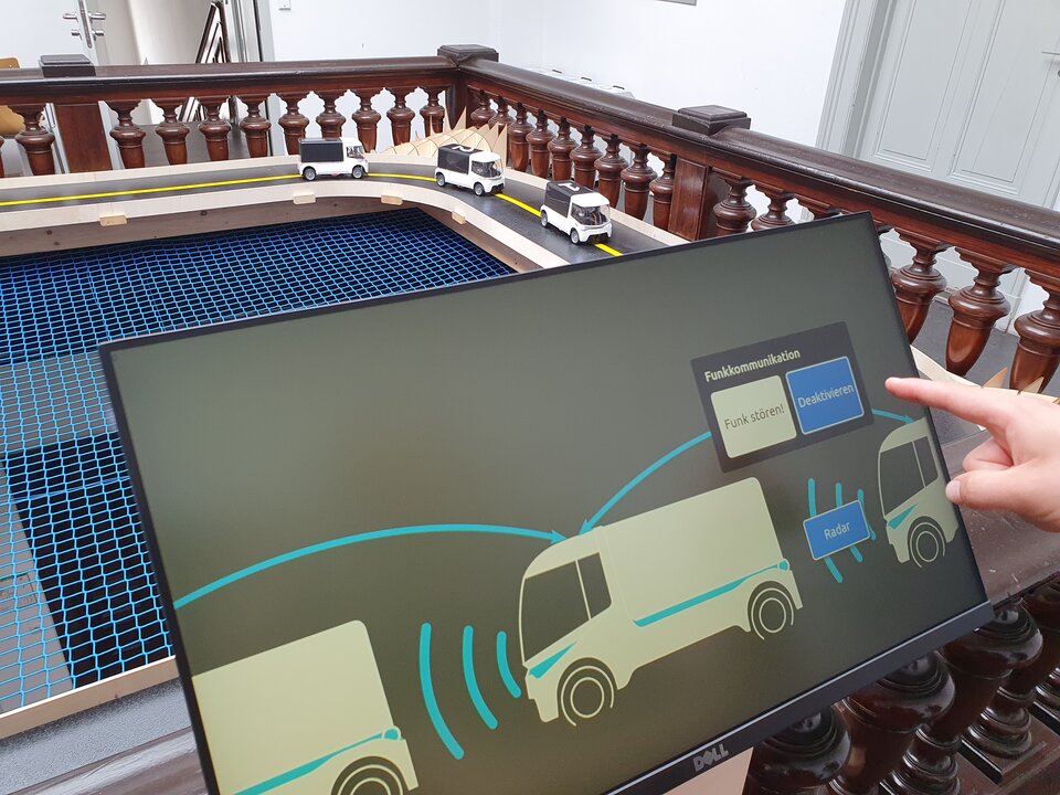 On the screen you can see cars communicating via radio. Behind the screen you can see a model highway with this same convoy.