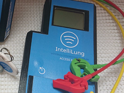There are 3 blue devices with one screen each. It says 'IntelliLung' and the function of the device. You can also see 3 colored cables in green, red and yellow, with a clip at the end.